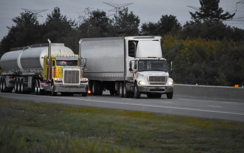 Two trailer trucks driving on the road surrounded by beautiful green trees