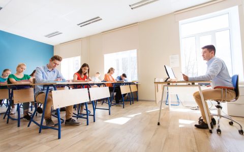 education, teaching, learning, technology and people concept - group of students writing school test and teacher with tablet pc computer in classroom