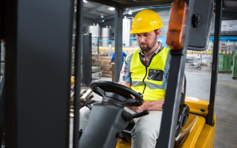 Young male worker sitting in forklift at warehouse